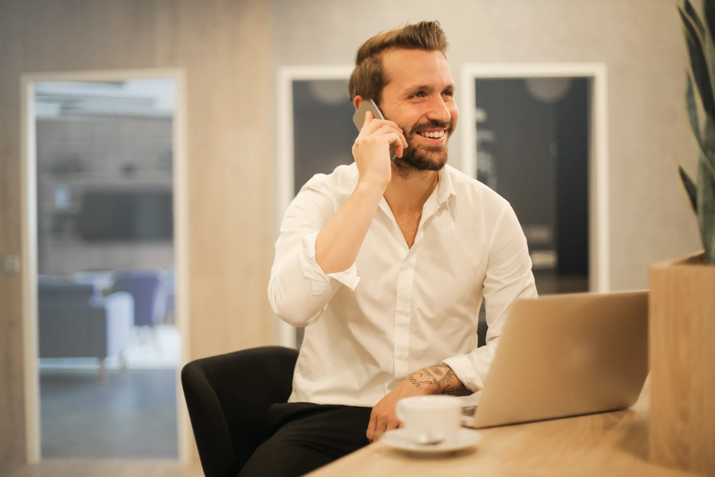 A happy male business owner talking on a smartphone while sitting on a chair.